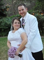 A man wearing a white suit and a woman wearing a white dress posing